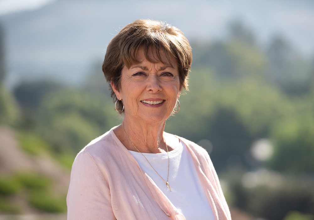 Woman with short brown hair and pink cardigan smiling outside